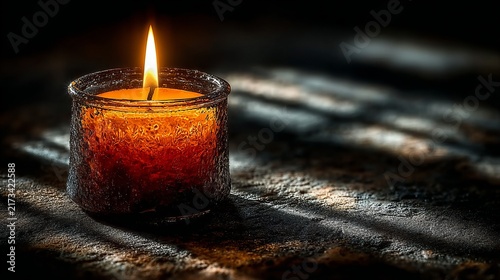 The warm, flickering glow of a solitary candle illuminates the room, casting intricate shadows upon the textured surface nearby during a peaceful evening