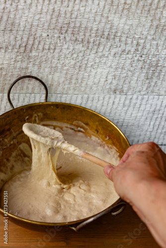 Stirring bread dough in an old brass bowl with a wooden spoon. Rustic charm, traditional baking.