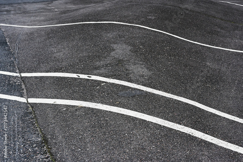 Abstract close-up of weathered asphalt marked with curved and irregular white road lines.