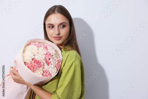 Smiling woman with bouquet of carnation flowers on light grey background. Spa...