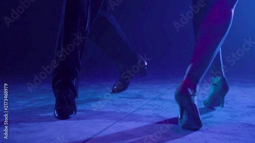 Professional couple performing elegant tango dance steps on dark stage
