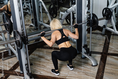 Athletic woman performing squats with barbell in gym