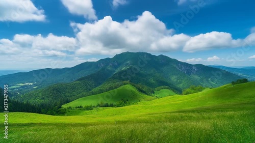 Lush green mountain valley with rolling hills under a bright blue sky with fluffy clouds