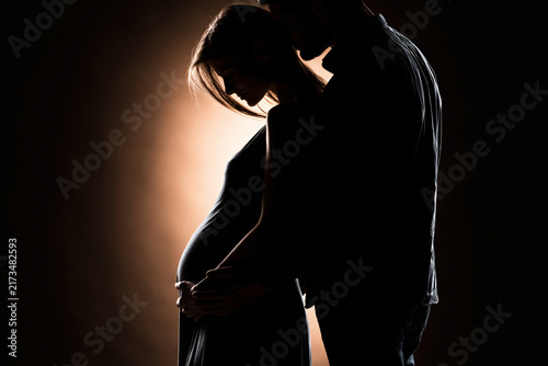 Partner hands tenderly placed on pregnant belly from behind