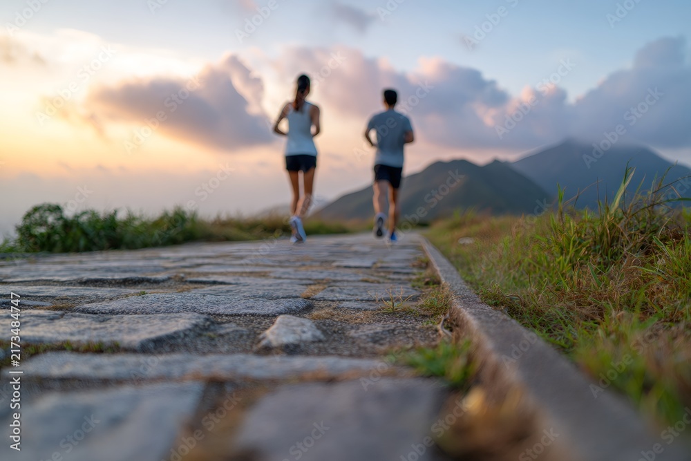 Obraz premium Stone trail with a couple jogging in the mountains at sunset. Outdoor fitness and active lifestyle. Focus on the path with blurred runners in the background