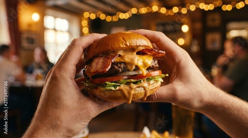 Hands hold a juicy cheeseburger with fresh lettuce and tomato in a warm restaurant setting. Fast food indulgence, comfort meal concept, casual dining experience, savory taste enjoyment.