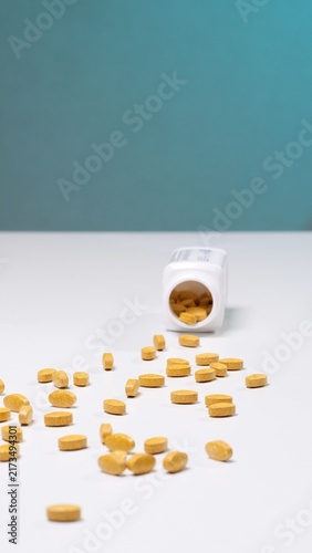 Konstfotografi Yellow oval pills spilling out from a white plastic bottle, scattered across a c