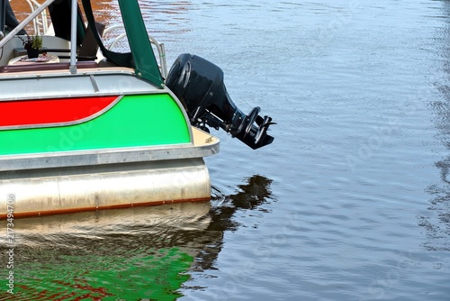 Cuadro en lienzo Black outboard motor mounted on a colorful pontoon boat on calm water