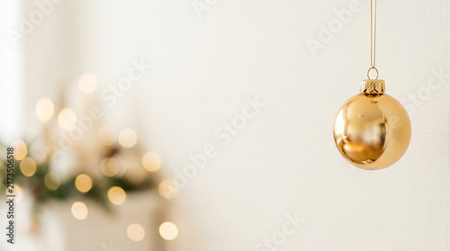 Elegant Gold Christmas Ornament Hanging Against a Soft Blurred Festive Holiday Background with Warm Glowing Bokeh Lights for Seasonal Decor