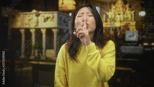 Cuadro en lienzo Woman finger to lips for silence in church building wearing yellow sweater; silence secrecy contemplation