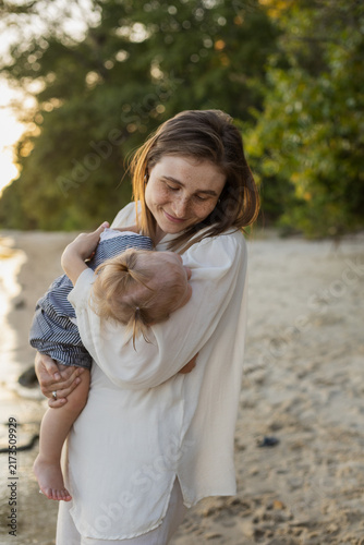 Cuadro en lienzo Mother tenderly holding her sleeping baby on a sandy beach at sunset