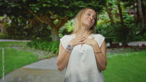 Fotografía Woman points thumb to herself in white blouse with wristwatch on park path in forest, playful smirk; self confidence pride