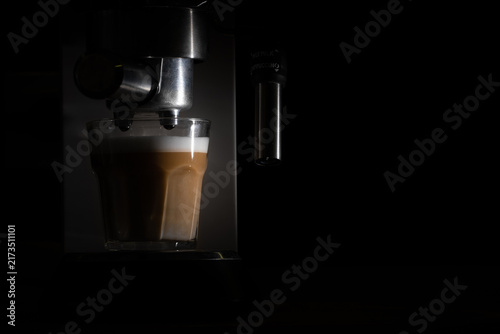 Close-up of a professional espresso machine preparing fresh coffee in a dark setting, with espresso flowing into a glass. Atmospheric coffee and beverage photography with dramatic low-key lighting.