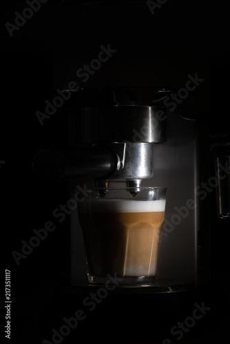 Close-up of a professional espresso machine preparing fresh coffee in a dark setting, with espresso flowing into a glass. Atmospheric coffee and beverage photography with dramatic low-key lighting.