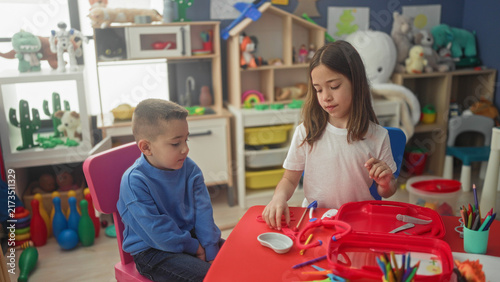 Foto Girl uses toy stethoscope and syringe on seated boy at a preschool play table in building; playful roleplay learning