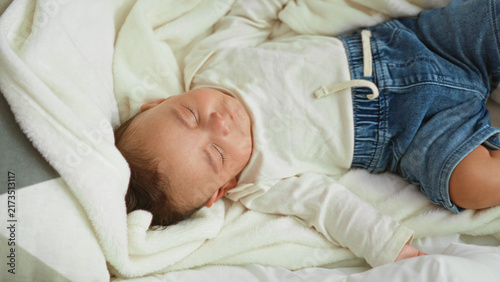 Konstfotografi Baby boy sleeping with closed eyes and hand on soft blanket on bed in building, wearing white shirt and denim shorts; peaceful comfort