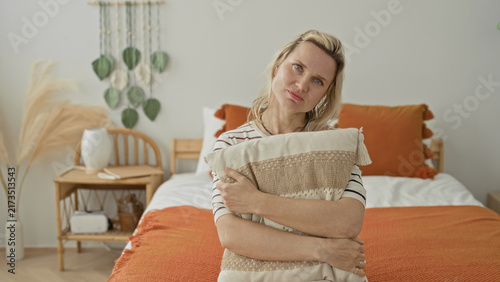 Fotografía Woman hugging pillow on bed inside a building, hands clasped over cushion and orange throw, seated in gentle posture; quiet contemplation solitude