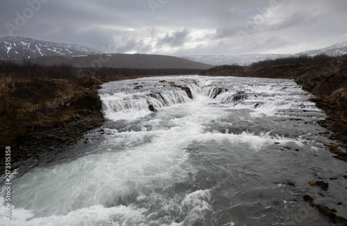 Cuadro en lienzo Waterfall flow over rocks in a river mountains and cloudy sky