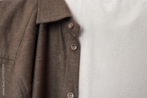 Close-up detail of a brown button-down shirt collar and buttons layered over light fabric.