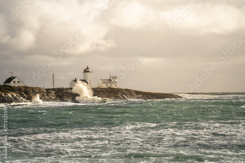 Foto Golden break in storm lights Langoytangen lighthouse and sea spray above restless green water in Norway for changing weather, atmospheric travel and warm coastal landscape stories