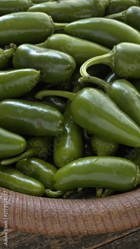 Jalapeño peppers heap close-up on a handmade dish. A brown plate of fresh green chilies on a dark, rustic wooden background. Table spin, vertical video.