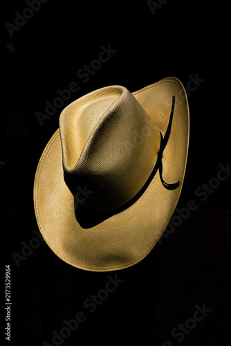 Western style cowboy hat has wide brim, leather tie band, crown form,  & straw weave with distinction & stiff qualities. Tipped forward hat shows off top crown.