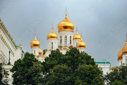 Canvas Print Golden onion domes of Orthodox cathedral rising above green trees under overcast