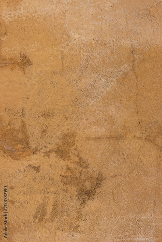 Full frame textured ochre cement wall surface featuring rough sandy patches, subtle stains, and weathered earthy tones, ideal for rustic exterior architectural backgrounds.