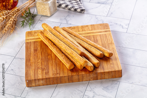 Obraz na płótnie Grissini breadsticks on wooden cutting board with rosemary and wheat ears