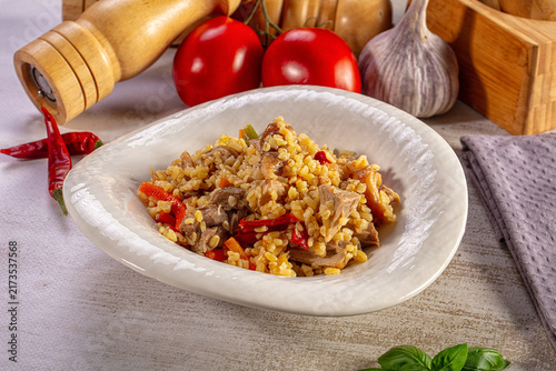 Foto Hearty bulgur pilaf with meat and vegetables served in a white bowl on a rustic