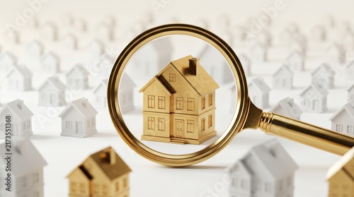 A single golden house is viewed through a magnifying glass among white toy houses on a white background.