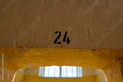 Obraz na płótnie Black painted digits twenty-four marking an old detention cell entrance, set against thick yellow paint on a rough stone arch with a bright blurred background