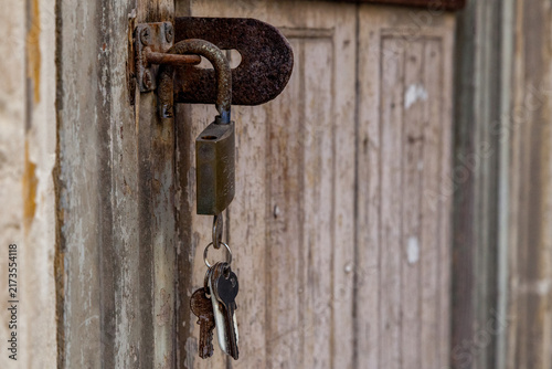 A rusty padlock and old keys hang from a weathered latch on a peeling wooden door in Valletta, Malta