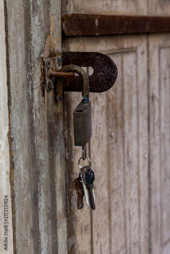 Bild auf Leinwand A rusty padlock and old keys hang from a weathered latch on a peeling wooden doo
