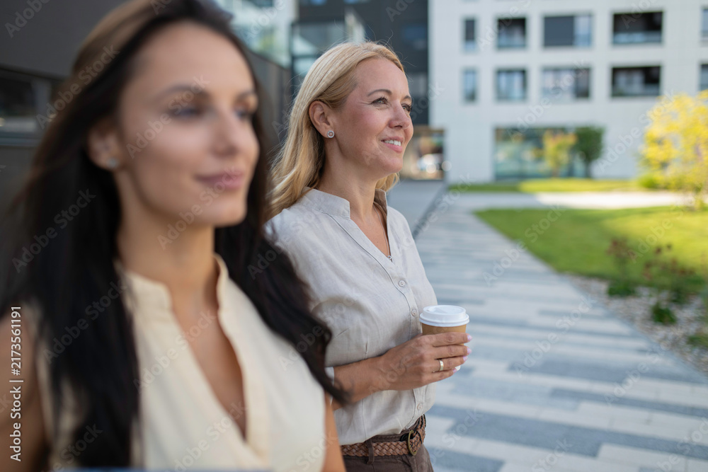 Fototapeta premium Businesswomen walking together holding coffee cups outdoors