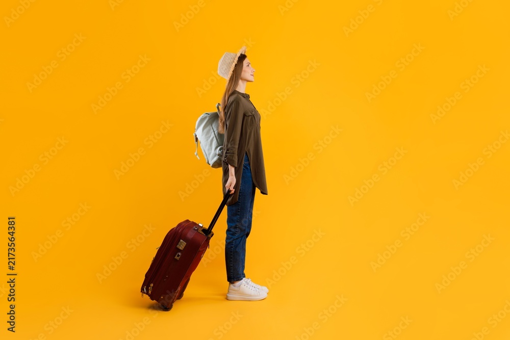 Naklejka premium Focused Young Caucasian Female With Backpack And Rolling Suitcase Preparing For Travel, Standing On Studio Yellow Background. Weight Loss Concept.