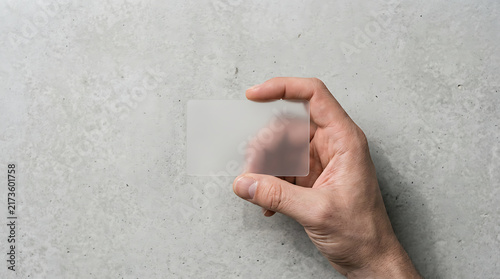 Male Hand Holding Blank Translucent Frosted Plastic Business Card Mockup on Grey Concrete Background, Top View Professional Identity Card Template for Branding and Membership Design Presentation
