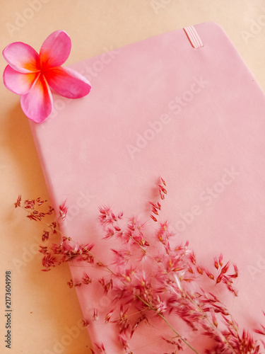 Pink notebook flat lay with frangipani flower and dry grass flowers on a pastel background