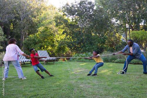 Fotografía African American family pulling long rope on backyard lawn, woman in pink shirt,