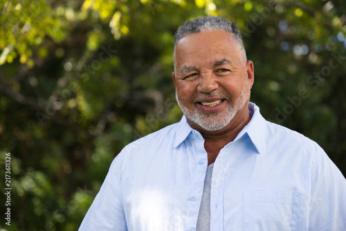 Senior African American man posing and smiling, looking left in park wearing blue shirt, gray tee