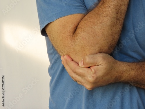 Fotografie Closeup of man in blue cotton t-shirt holding his elbow in pain