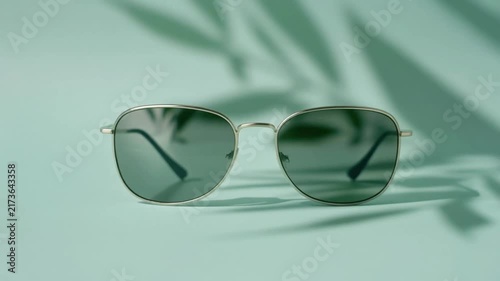 Silver rimmed sunglasses resting on soft pastel background with moving leaf shadow in video footage clip
