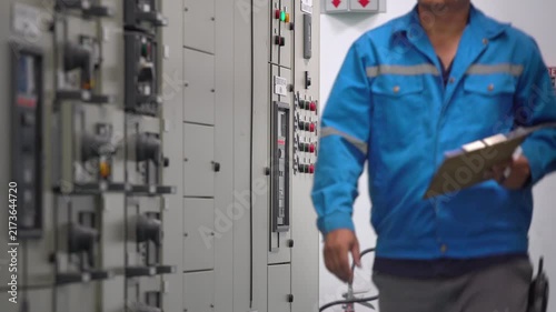 Engineer using electrical measurement equipment to inspect power parameters inside a substation control room, illustrating electricity distribution, power monitoring, industrial technology, energy eff