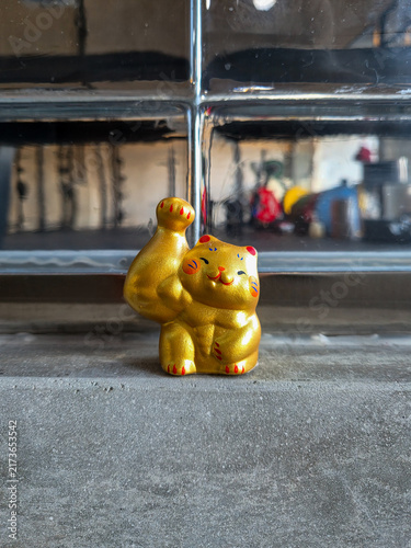 Funny muscular golden Maneki-neko lucky cat figurine sitting on a concrete ledge