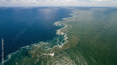 Aerial view of two distinct bodies of water meeting, showcasing a stark contrast between clear blue ocean and murky green river sediment
