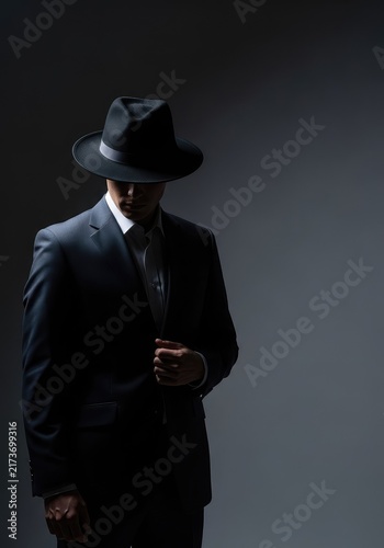 Sharp formal attire and a vintage fedora hat appear in moody low lighting, creating a mysterious atmosphere with cinematic deep shadows, contrast, retro, gritty