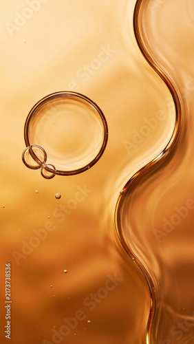 Top view of smooth wavy golden cosmetic oil with a single prominent circular bubble transparent cosmetic overhead abstract skincare hyaluronic