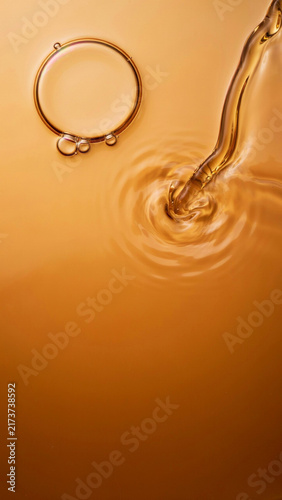 Pouring golden cosmetic oil into a rippling pool next to a floating circular air bubble with cosmetic transparent skincare hydration moisturizer