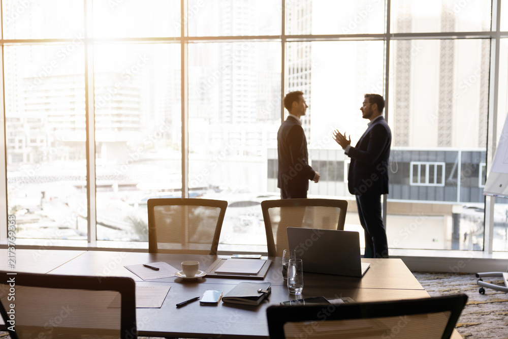 Obraz premium Businessmen talking in office boardroom, discuss project strategy, planning business decisions standing next to window overlooking city. Corporate communication, professional negotiation, partnership