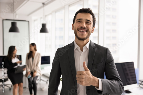 Portrait smiling Middle-eastern businessman giving thumbs up in corporate office, represents business achievement, success and approval, express positive feedback of customer services. HR, employment
